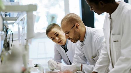 Scientists gathering around a desk station in a lab 